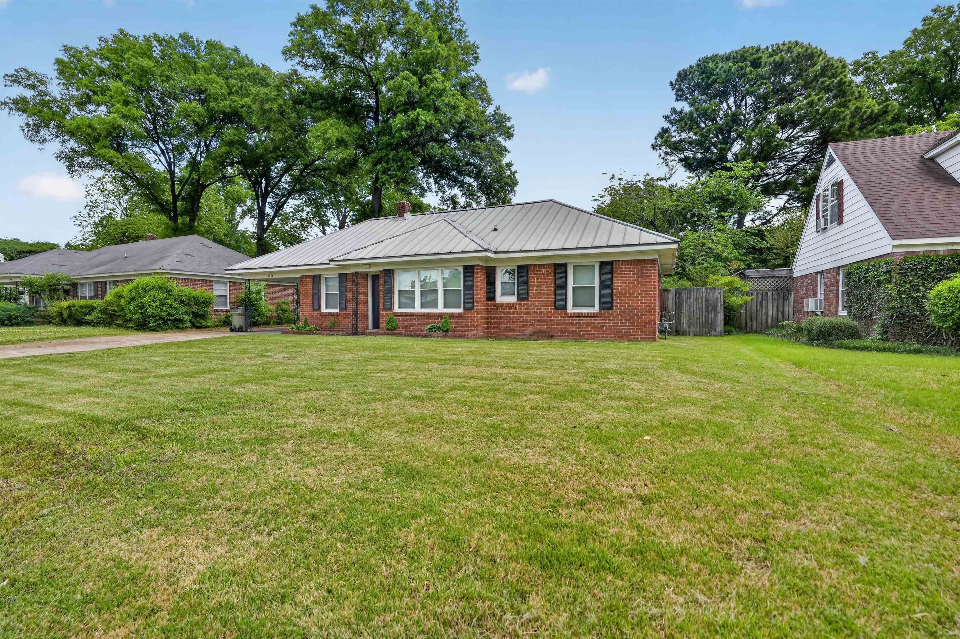 1514 Mt Moriah Road Memphis, TN 38117 - Photo 11 of 34 Brick exterior home featuring a metal roof, black louvered shutters, and a well-maintained front lawn