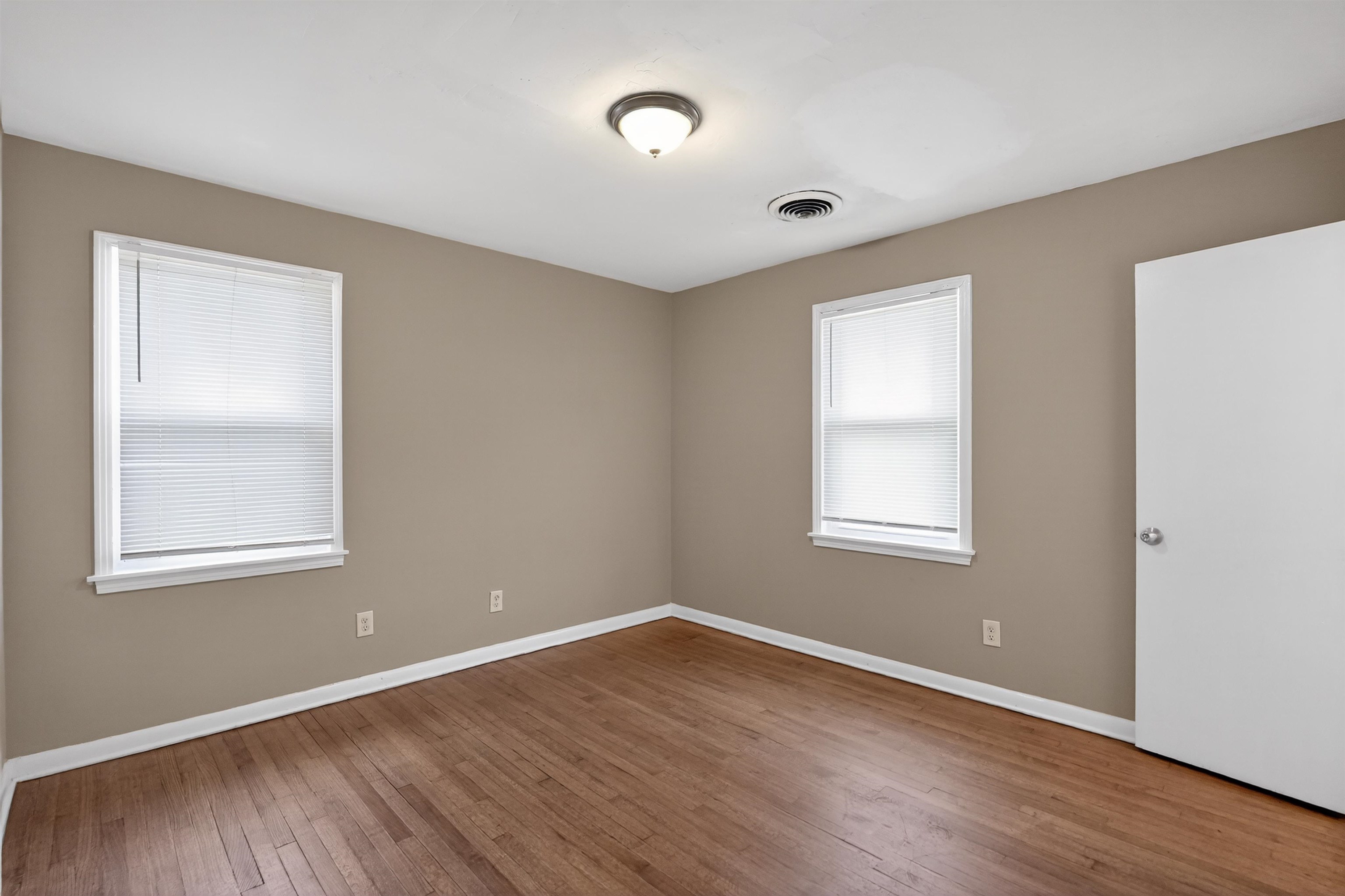 1514 Mt Moriah Road Memphis, TN 38117 - Photo 16 of 34 Spacious room featuring wood-finish flooring, neutral-toned walls, two windows with blinds, a ceiling-mounted light fixture, and white trim