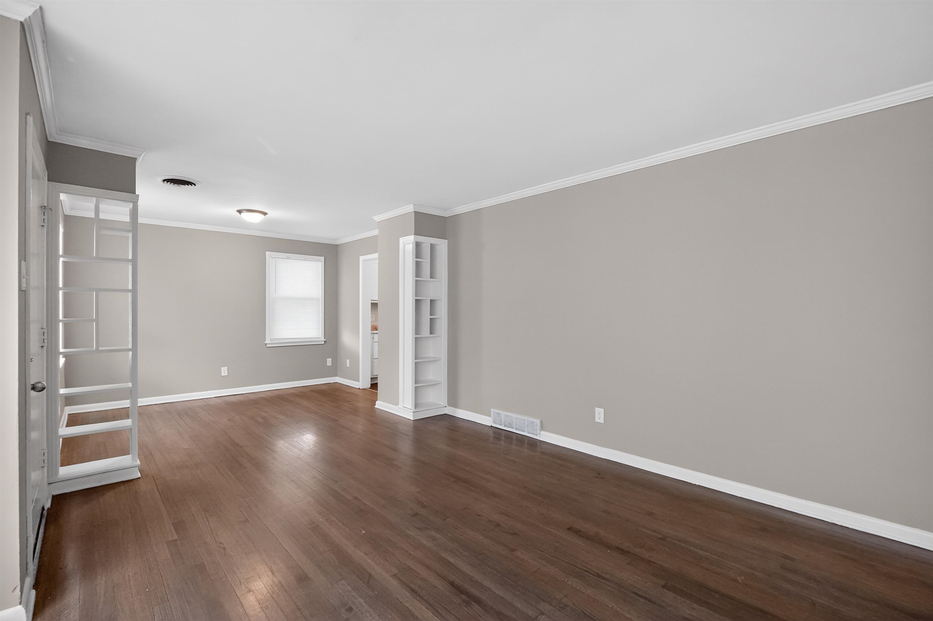 1514 Mt Moriah Road Memphis, TN 38117 - Photo 17 of 34 Spacious living area featuring wood-finish flooring, light gray wall paint, white crown molding, and two built-in shelving units