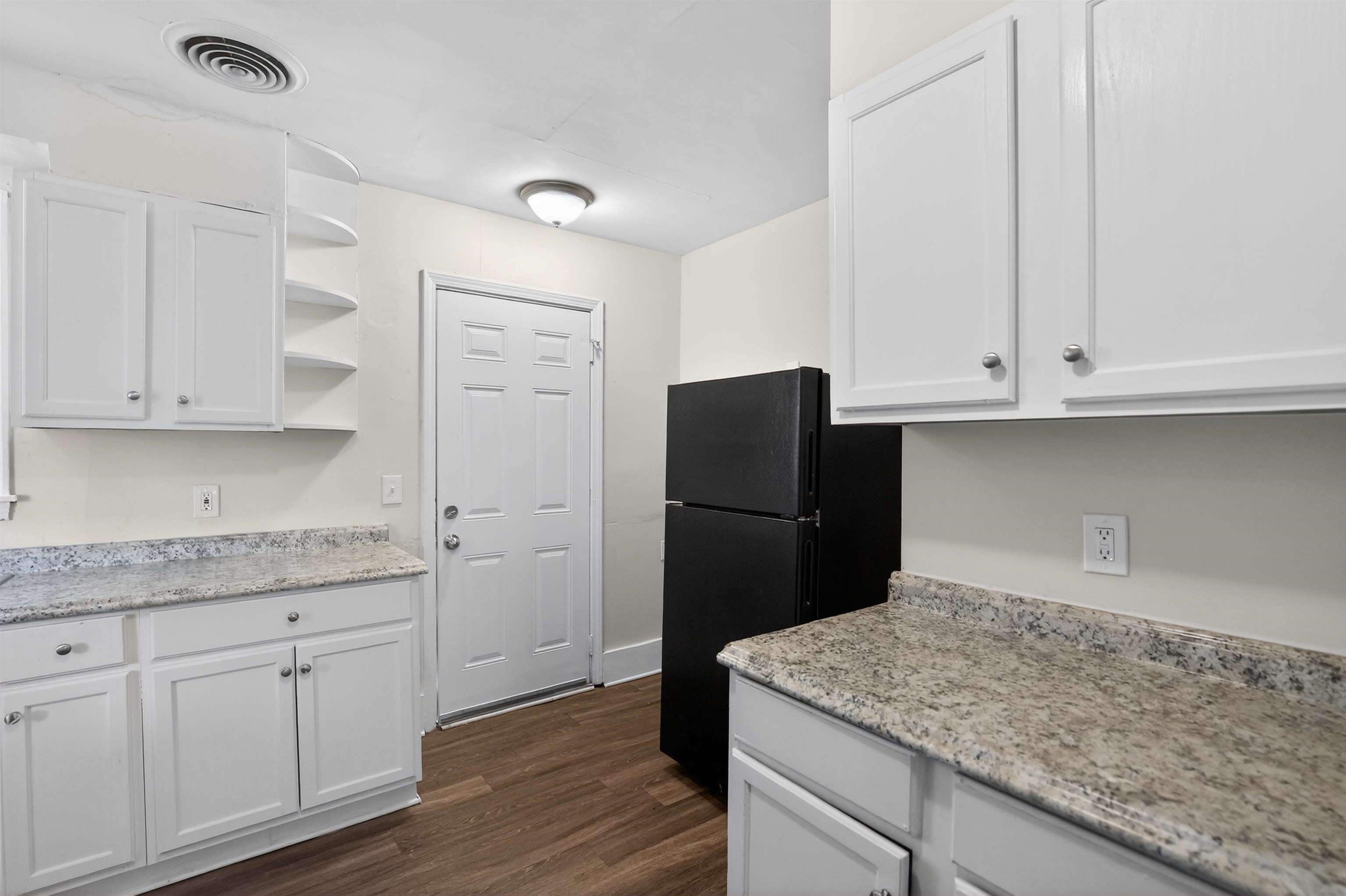 1514 Mt Moriah Road Memphis, TN 38117 - Photo 24 of 34 Kitchen area featuring white cabinetry with silver hardware, speckled countertops, wood-finish flooring, a white paneled door, and a black refrigerator