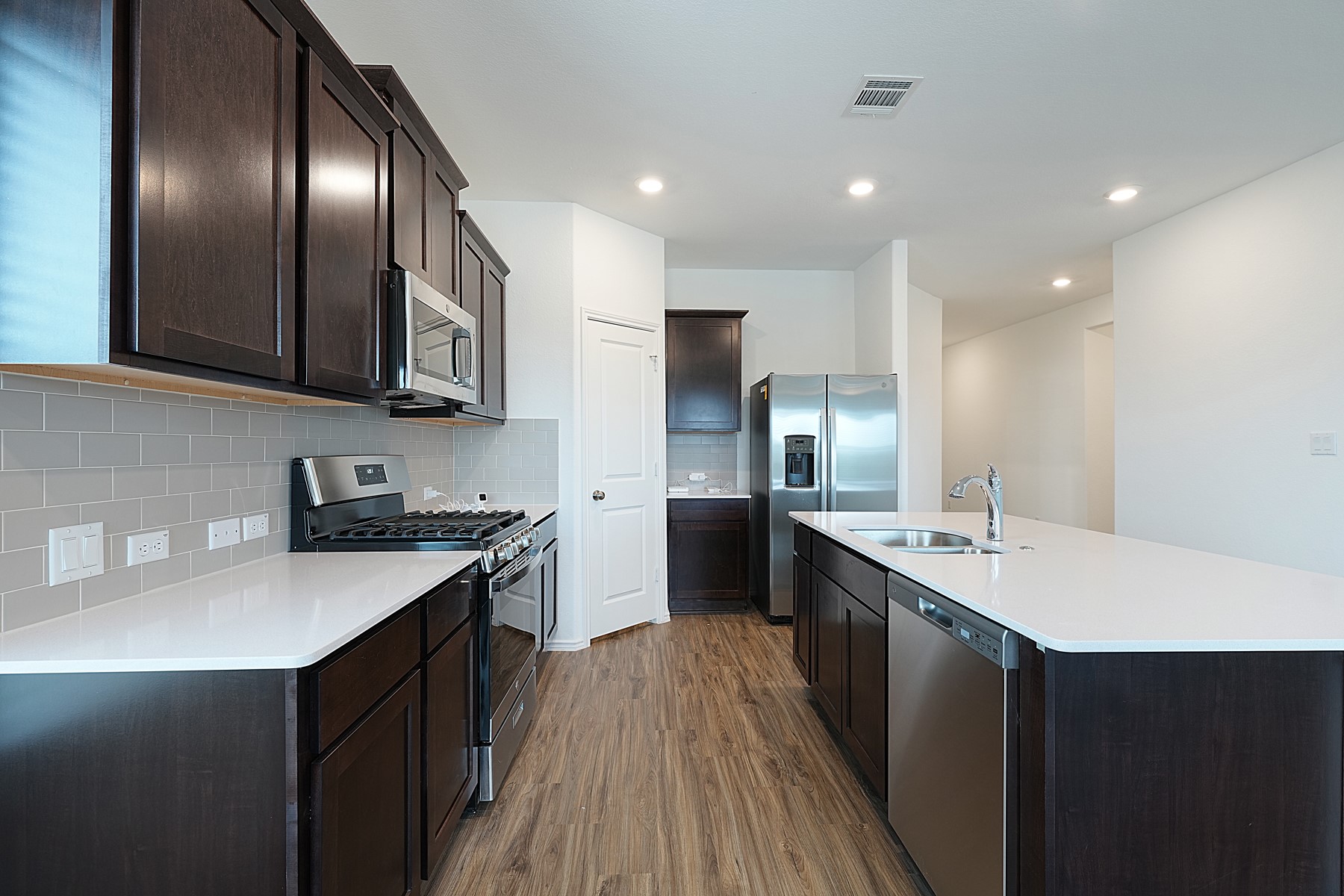 932 Mallow Road Leander, TX 78641 - Photo 19 of 34 Modern kitchen with white quartz countertops and ample dark wood cabinetry.
