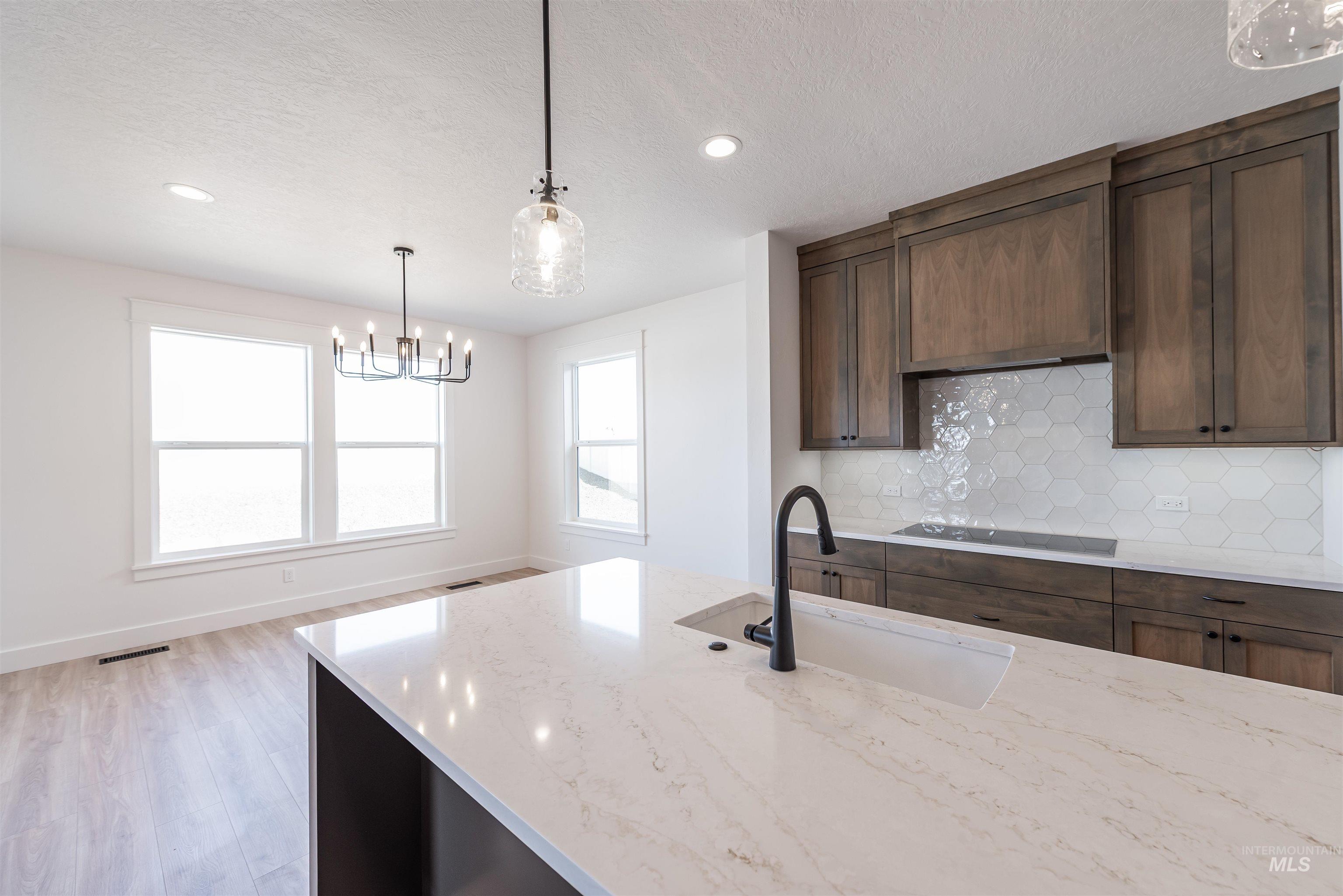 410 South Diesel Way Boise, ID 83716 - Photo 11 of 49 Kitchen featuring light stone countertops, hanging lights, tasteful backsplash, light wood finished floors, and dark wood finish cabinetry