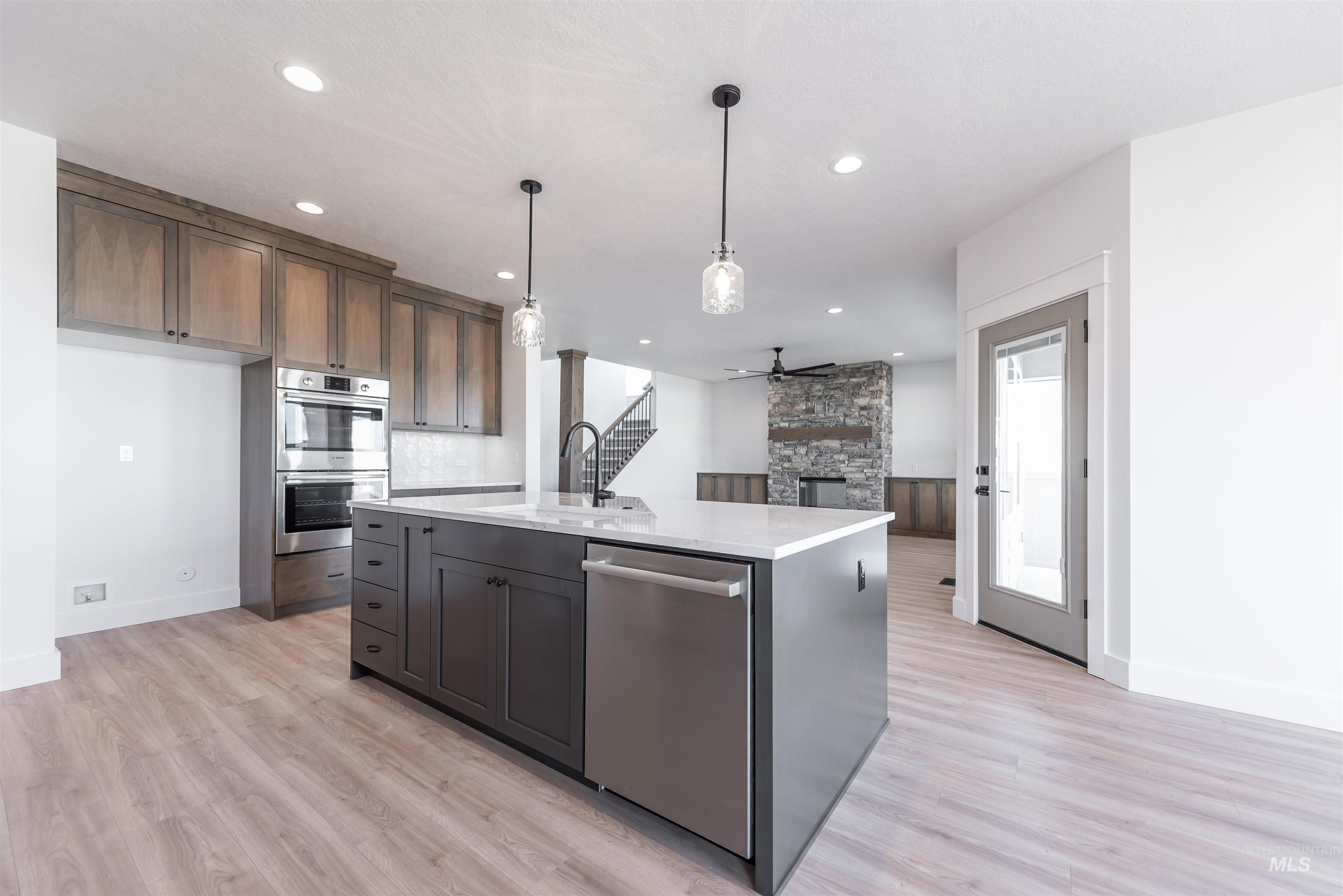 410 South Diesel Way Boise, ID 83716 - Photo 13 of 49 Kitchen with a stone fireplace, stainless steel appliances, a ceiling fan, an island with sink, and light wood-style floors