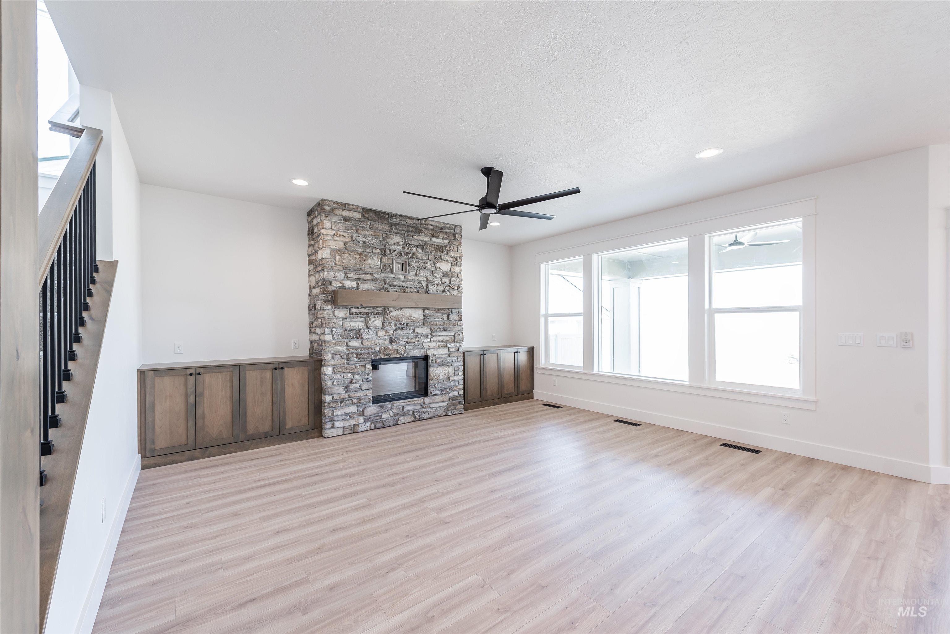 410 South Diesel Way Boise, ID 83716 - Photo 4 of 49 Unfurnished living room with light wood-type flooring, a stone fireplace, and a ceiling fan