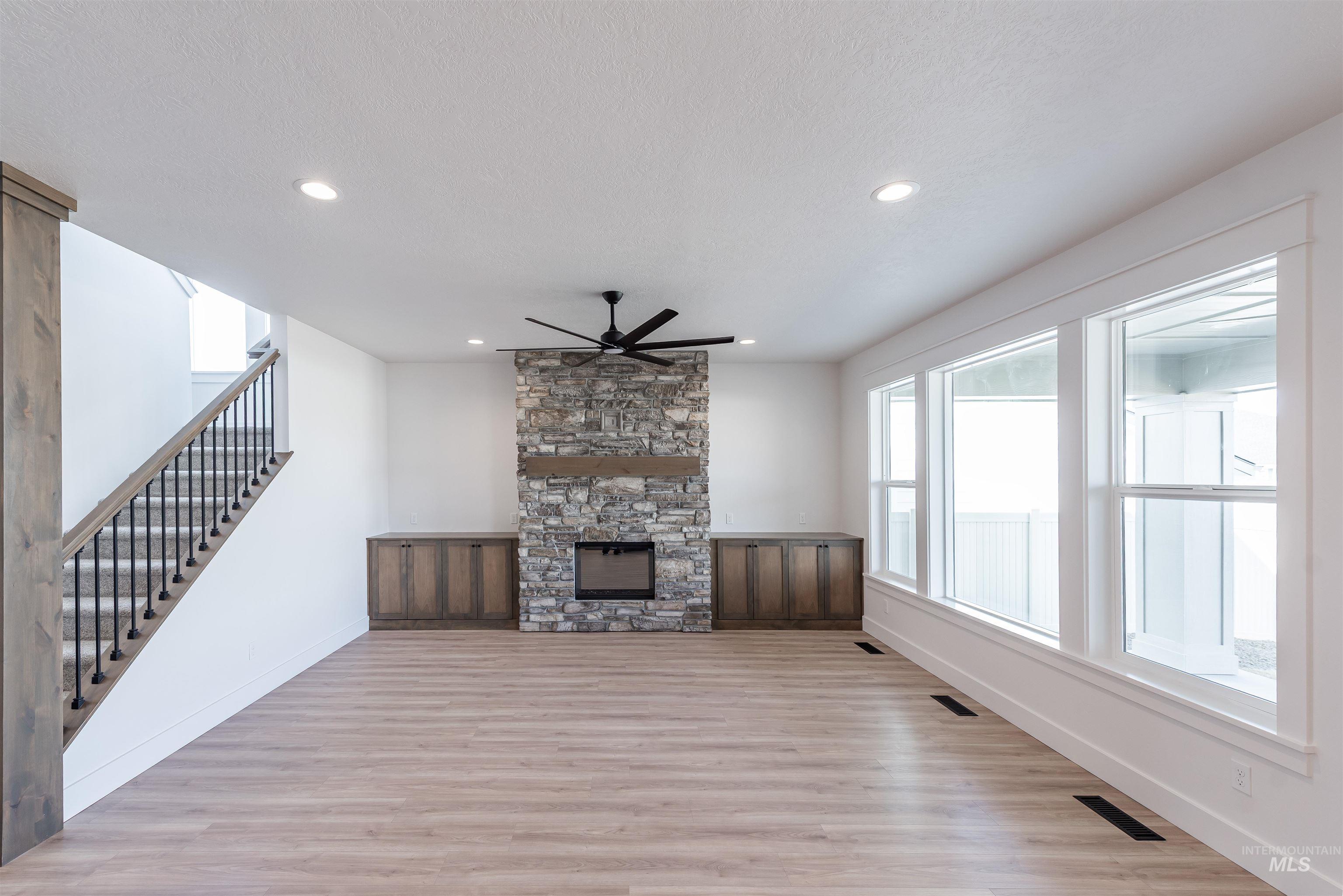 410 South Diesel Way Boise, ID 83716 - Photo 5 of 49 Unfurnished living room with a stone fireplace, light wood-style flooring, ceiling fan, recessed lighting, and a textured ceiling