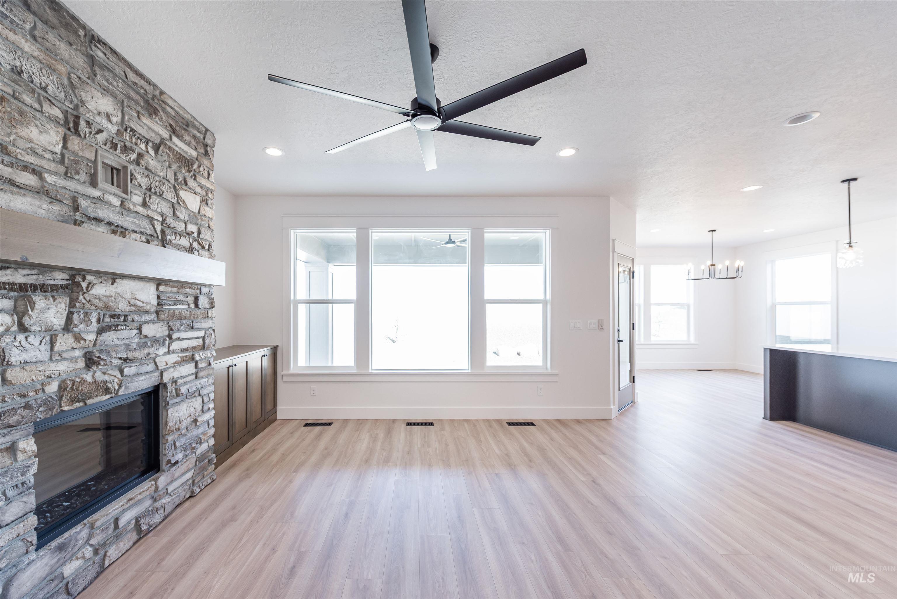 410 South Diesel Way Boise, ID 83716 - Photo 6 of 49 Unfurnished living room with light wood-style flooring, a stone fireplace, ceiling fan, a chandelier, and a textured ceiling