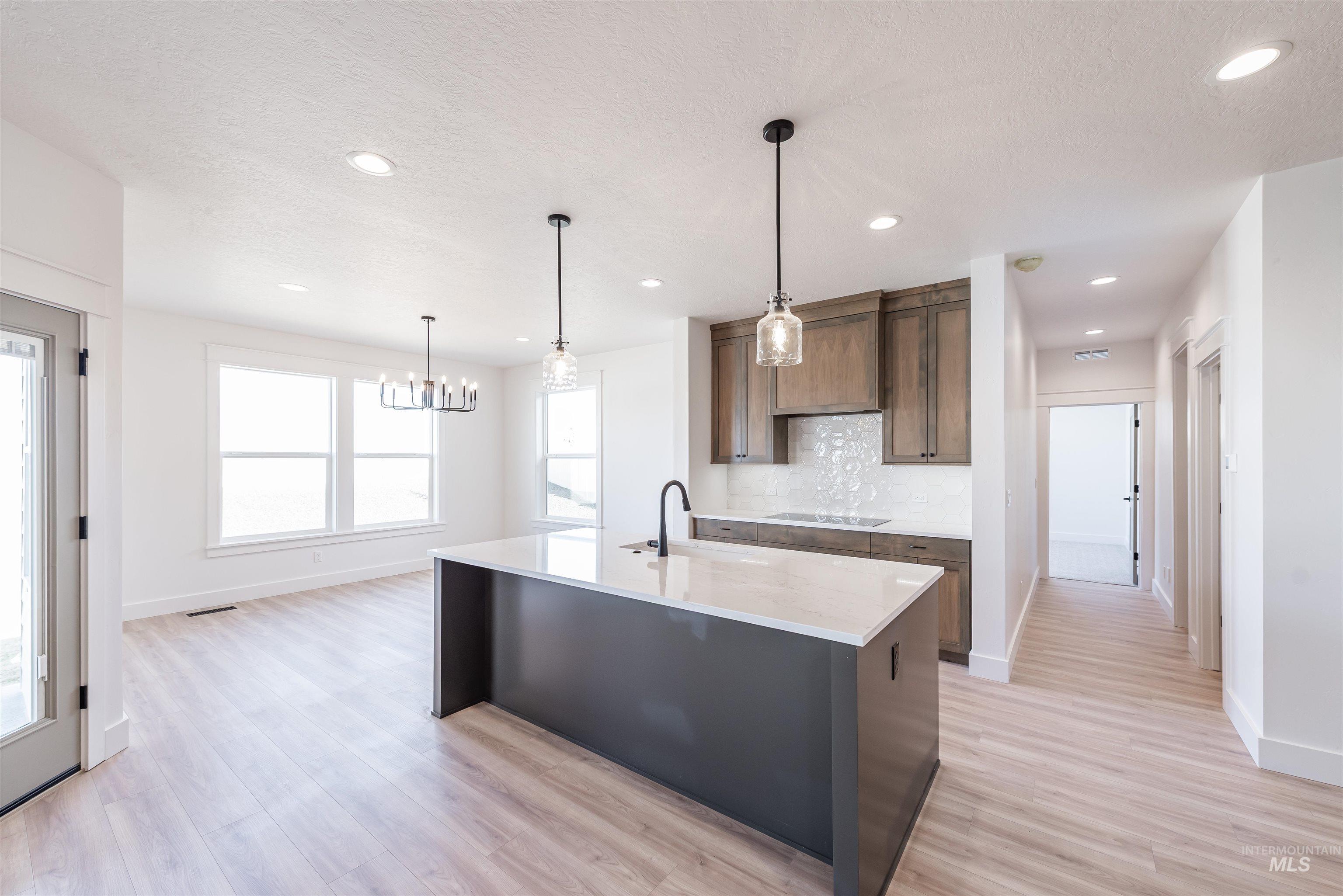 410 South Diesel Way Boise, ID 83716 - Photo 8 of 49 Kitchen featuring light stone countertops, a center island with sink, light wood-style floors, suspended lighting, and backsplash
