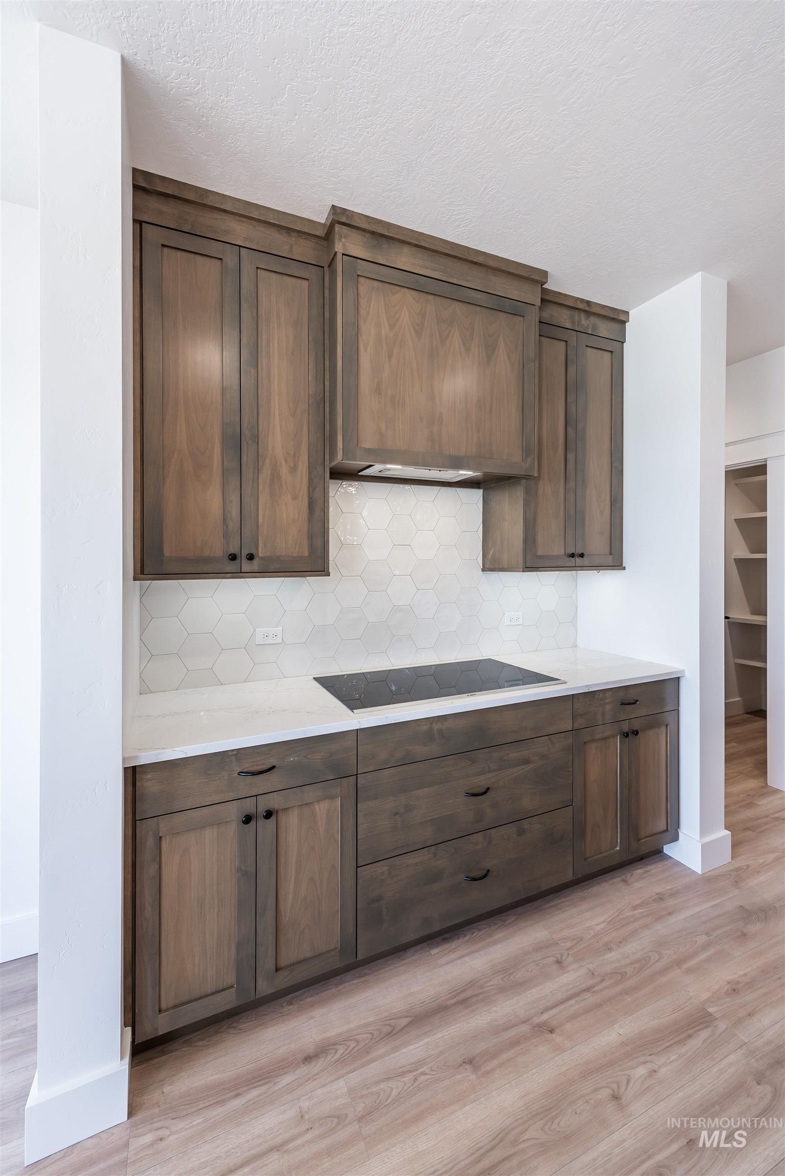 410 South Diesel Way Boise, ID 83716 - Photo 10 of 49 Kitchen featuring decorative backsplash, dark wood finish cabinets, light wood-style floors, light stone counters, and black electric cooktop