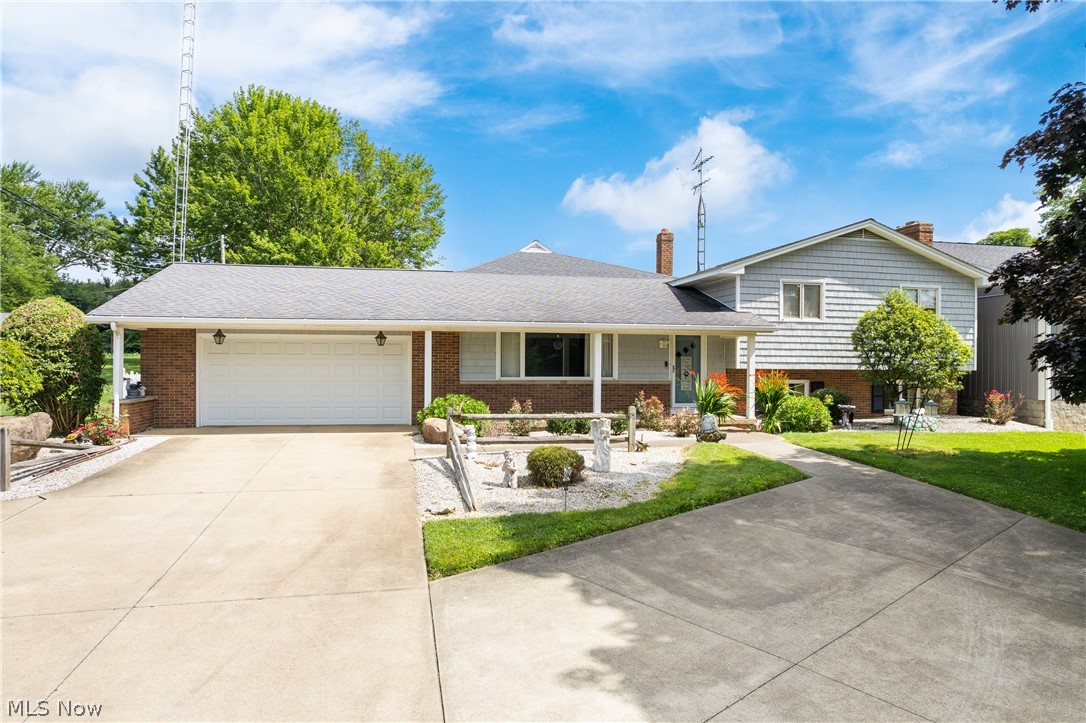 Split level home featuring a porch, driveway, an attached garage, a chimney, and brick siding