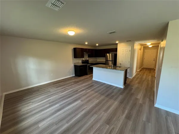 a view of kitchen and empty room with wooden floor