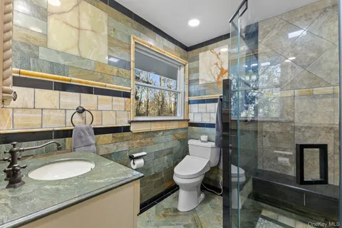 a bathroom with a granite countertop sink a toilet a mirror and shower
