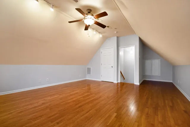 a view of an empty room with wooden floor and a ceiling fan