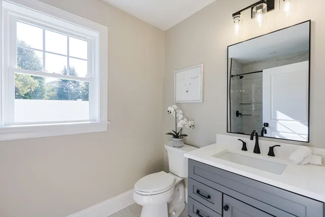 a bathroom with a toilet a sink a mirror a window and vanity