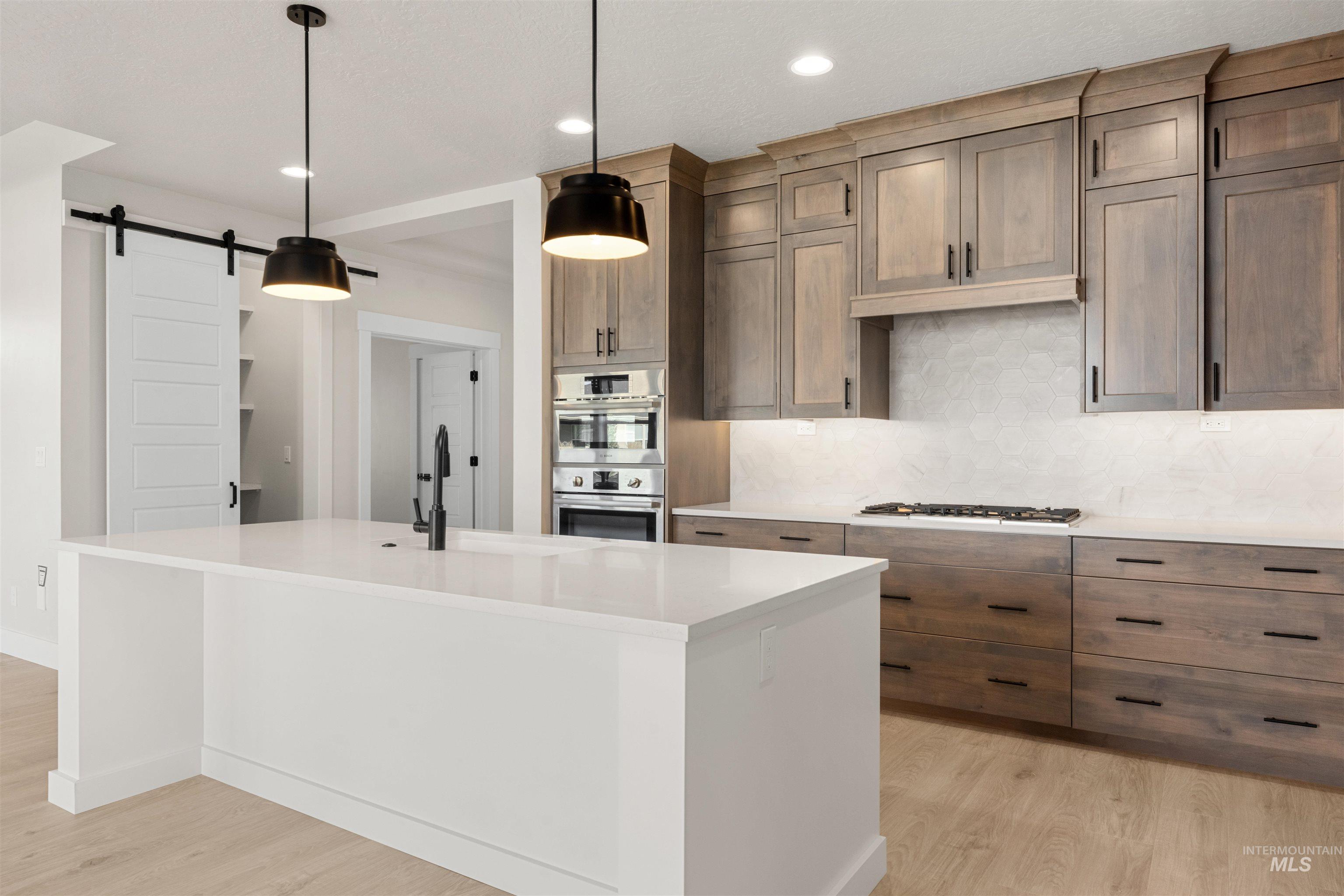8076 Tandy Cv Street Middleton, ID 83644 - Photo 10 of 41 Two tone kitchen featuring tasteful backsplash, light wood finished floors, a kitchen island with sink, stainless steel appliances, and a barn door