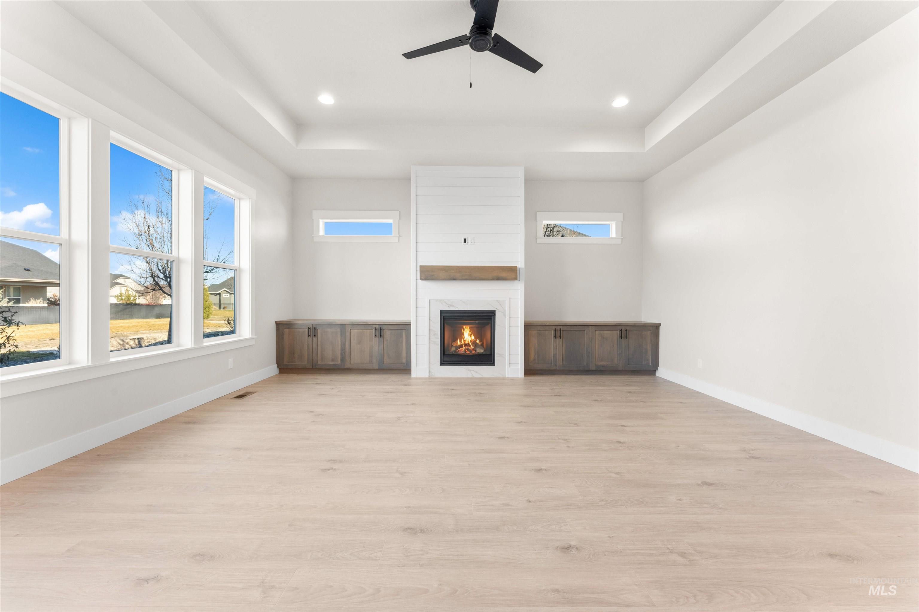 8076 Tandy Cv Street Middleton, ID 83644 - Photo 2 of 41 Unfurnished living room featuring a tray ceiling, ceiling fan, a fireplace, light wood-style floors, and recessed lighting