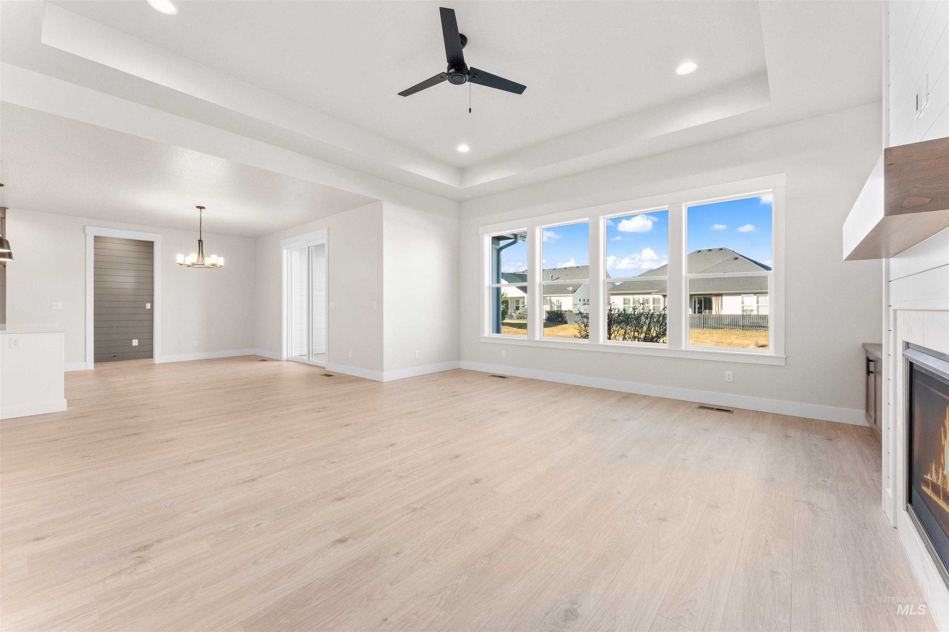 8076 Tandy Cv Street Middleton, ID 83644 - Photo 3 of 41 Unfurnished living room with ceiling fan, light wood finished floors, a chandelier, a glass covered fireplace, and a raised ceiling