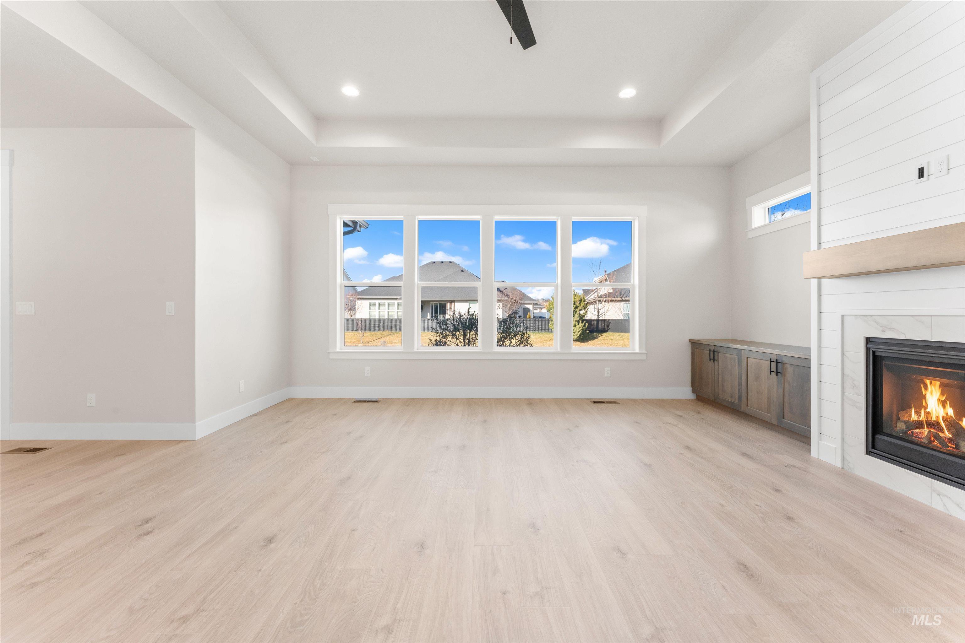 8076 Tandy Cv Street Middleton, ID 83644 - Photo 4 of 41 Unfurnished living room with a fireplace, light wood-style floors, a raised ceiling, plenty of natural light, and ceiling fan