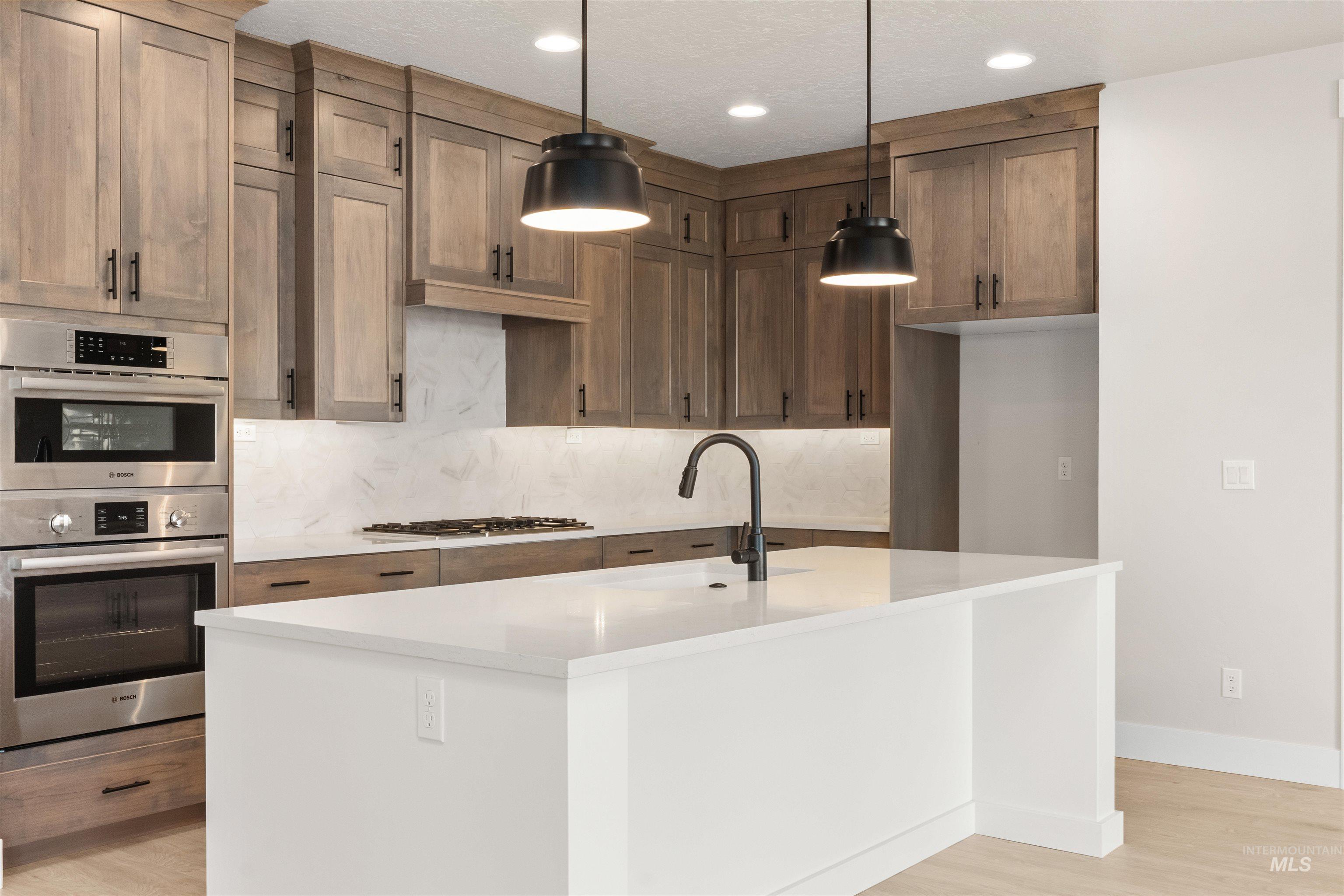 8076 Tandy Cv Street Middleton, ID 83644 - Photo 7 of 41 Kitchen featuring a center island with sink, stainless steel appliances, light stone counters, decorative backsplash, and light wood finished floors