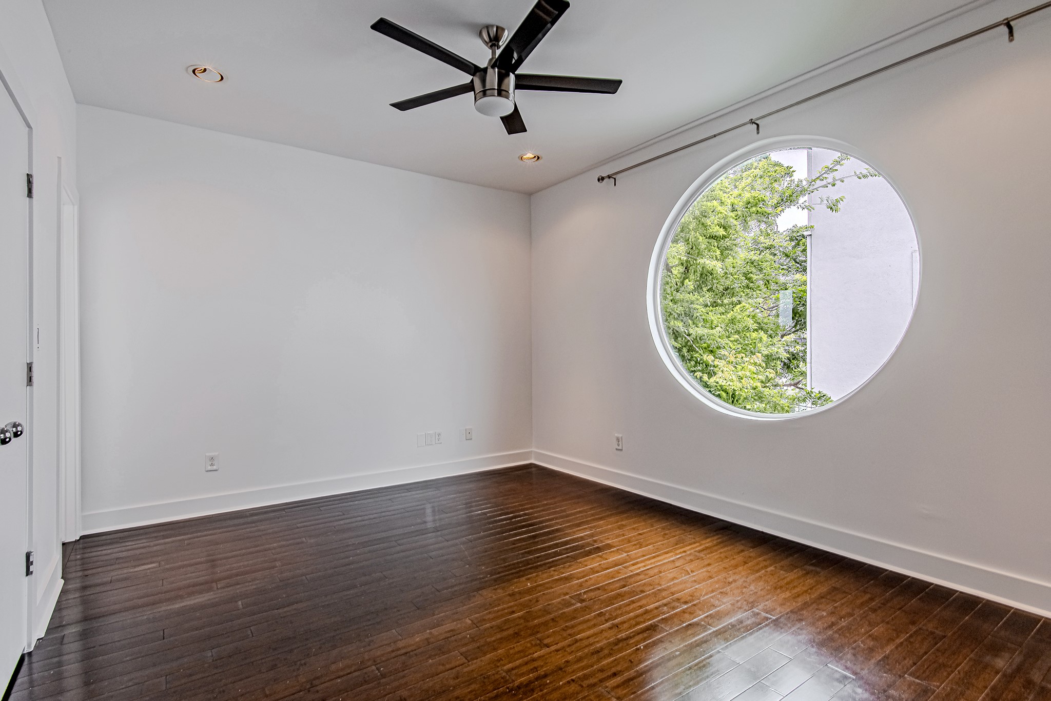 2025 Colquitt Street, Unit E Houston, TX 77098 - Photo 22 of 29 Secondary bedroom with distinctive circular window and warm wood flooring.