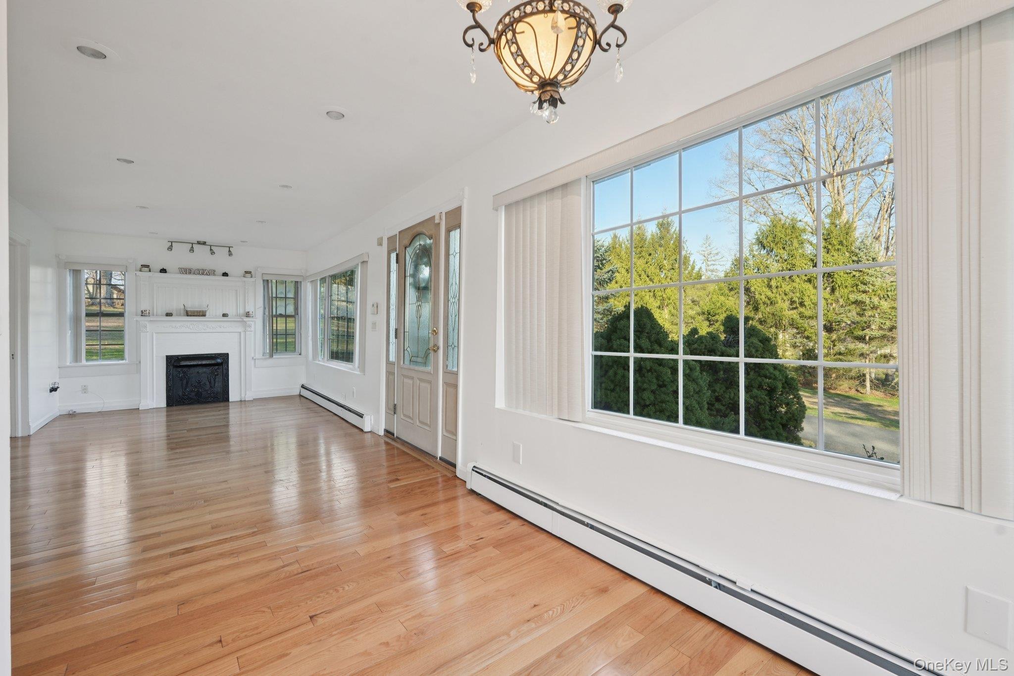 17 Pine Hill Road Highland Mills, NY 10930 - Photo 4 of 35 Unfurnished living room with baseboard heating, a baseboard heating unit, a fireplace, light wood finished floors, and suspended lighting