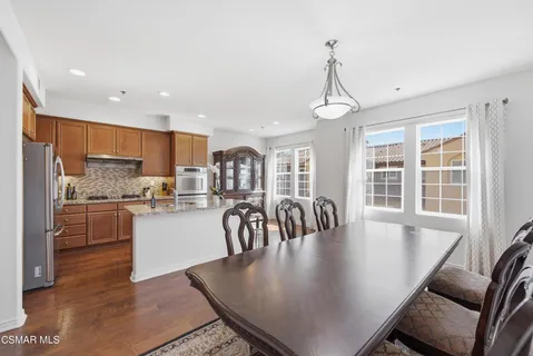 a dining room with stainless steel appliances granite countertop a table chairs a sink dishwasher a kitchen island with wooden cabinets and floor