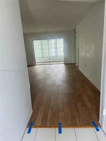 a view of an empty room with wooden floor and fan