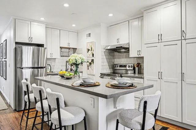 a kitchen with stainless steel appliances granite countertop a dining table chairs and white cabinets
