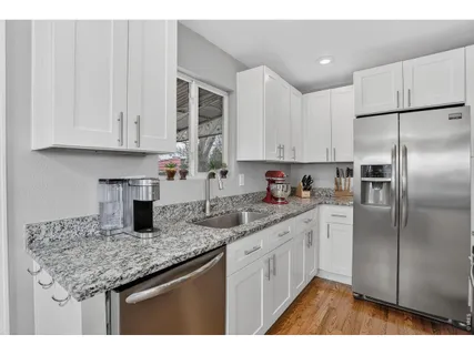 a kitchen with stainless steel appliances granite countertop a sink dishwasher a refrigerator and white cabinets with wooden floor