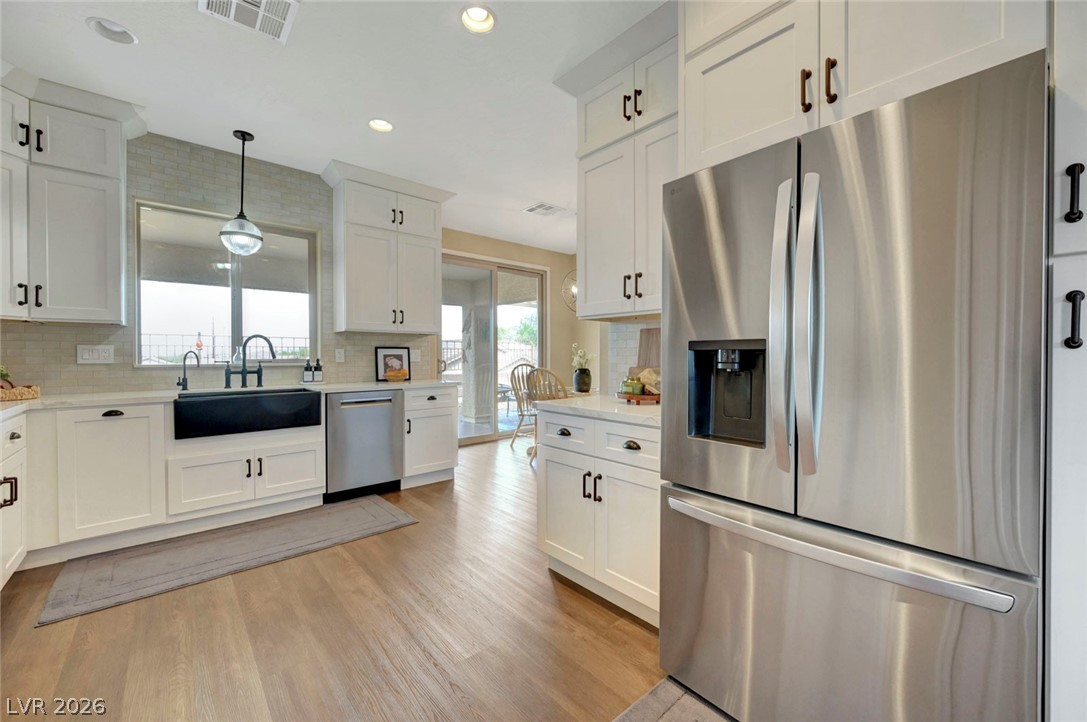 2700 Rue Montpellier Avenue Henderson, NV 89044 - Photo 16 of 39 Kitchen featuring stainless steel appliances, white cabinetry, light wood-style floors, hanging light fixtures, and backsplash