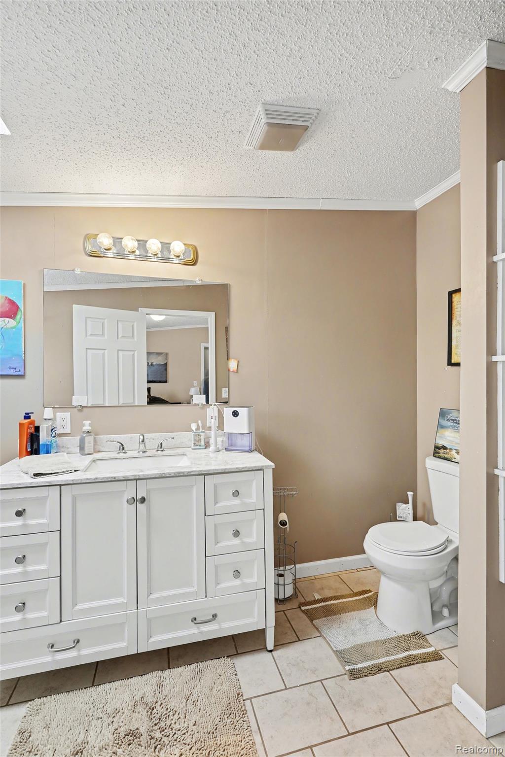 4458 Palms Road Casco, MI 48064 - Photo 18 of 32 Half bathroom featuring vanity, light tile patterned flooring, a textured ceiling, and crown molding