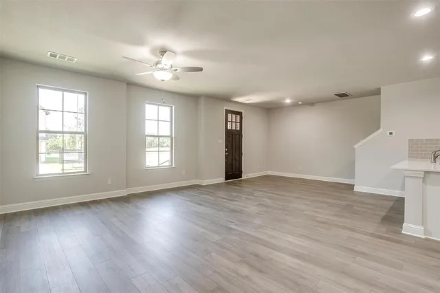 a view of an empty room with wooden floor and a ceiling fan
