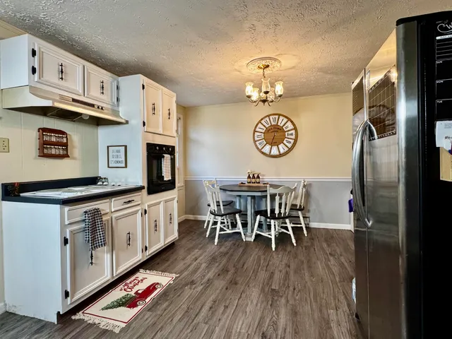 a kitchen with stainless steel appliances granite countertop a stove top oven a refrigerator a dining table and chairs with wooden floor