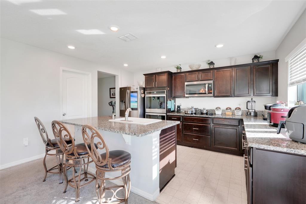 2111 Ficus Street Mascotte, FL 34753 - Photo 9 of 24 a kitchen with stainless steel appliances kitchen island granite countertop a stove top oven a sink a dining table and chairs