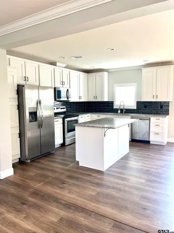 a kitchen with stainless steel appliances granite countertop a stove top oven a refrigerator and white cabinets