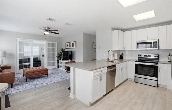 a kitchen with stainless steel appliances granite countertop a stove top oven a sink a refrigerator white cabinets and couches with wooden floor