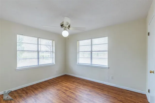 an empty room with wooden floor chandelier fan and windows