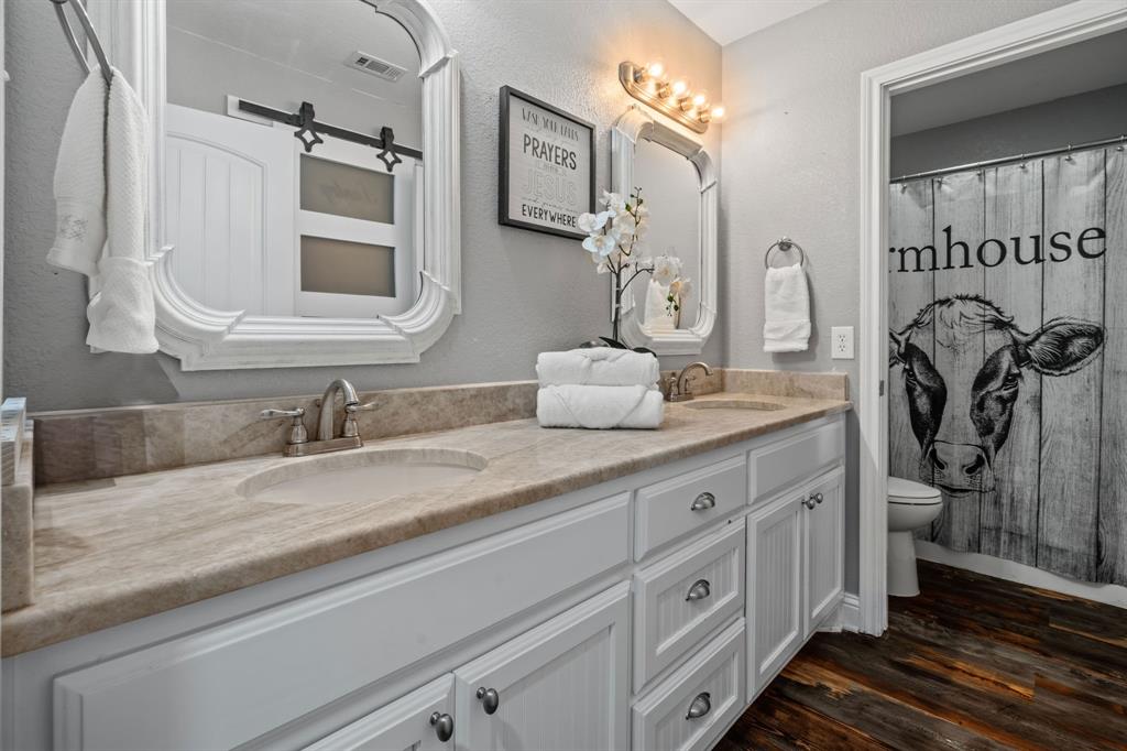 175 Porter Road Bartonville, TX 76226 - Photo 24 of 40 Bright, beautifully updated ensuite featuring dual sinks, framed mirrors, fresh finishes, warm farmhouse-inspired luxury vinyl floors, and shower with tub.