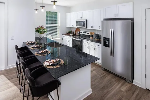 a kitchen with stainless steel appliances granite countertop a refrigerator a stove a sink dishwasher and a dining table with wooden floor