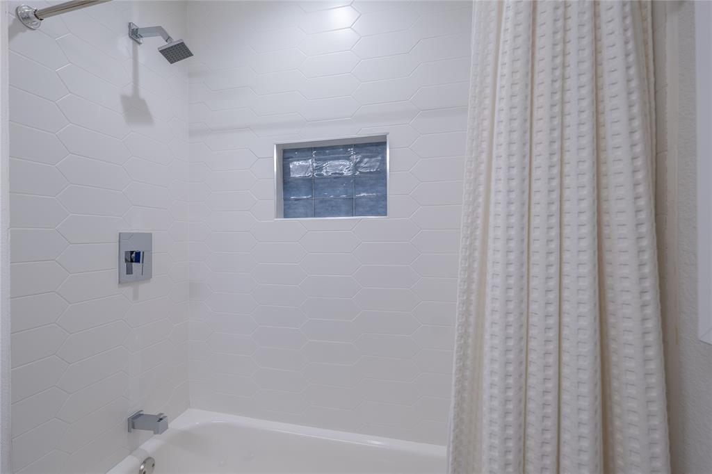 864 Peavy Road Dallas, TX 75218 - Photo 14 of 21 Bathtub with white subway tile surround, chrome fixtures, and a recessed niche with blue tile accents