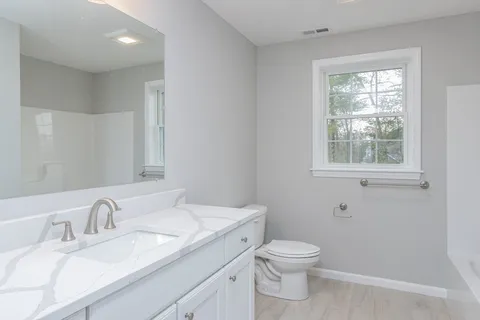a bathroom with a granite countertop toilet a sink a mirror and a window