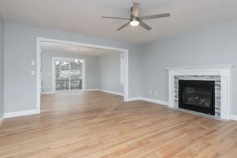 an empty room with wooden floor a ceiling fan a fireplace and windows