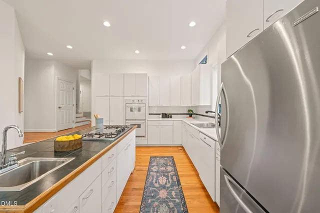 a kitchen with stainless steel appliances granite countertop a refrigerator a sink dishwasher and white cabinets with wooden floor