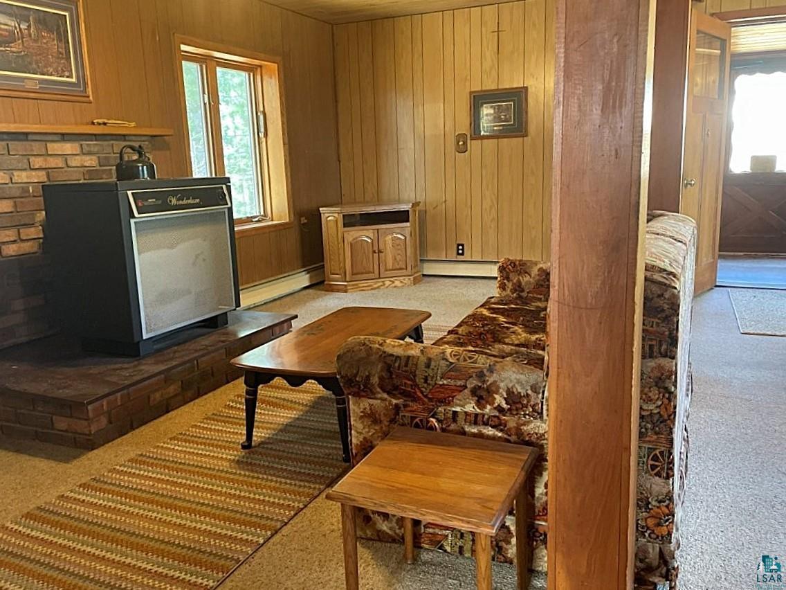 1480 Maijala Road Ely, MN 55731 - Photo 18 of 58 Living area featuring paneling, carpet flooring, a brick hearth, and baseboard hot water heating