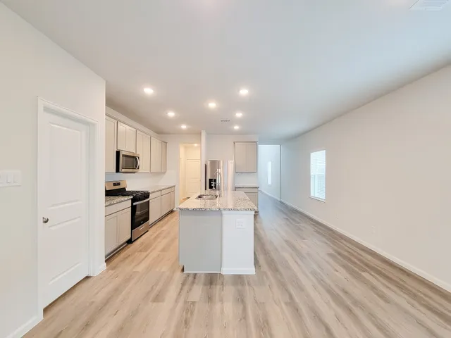 a large kitchen with kitchen island a sink dishwasher stove and white cabinets with wooden floor
