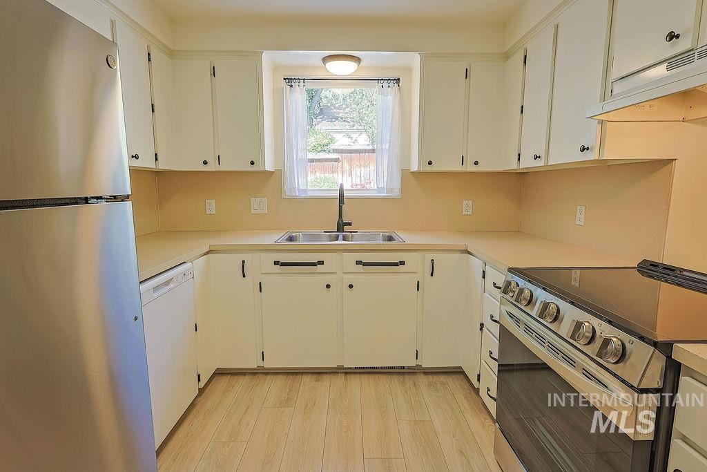 640 Morrison Street Twin Falls, ID 83301 - Photo 9 of 30 U-shaped kitchen with light wood-finish flooring, white cabinetry, a double basin stainless steel sink with a black faucet, and light-toned countertops