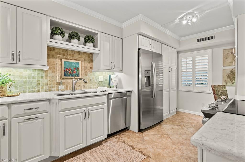 4155 Crayton Road, Unit 107 Naples, FL 34103 - Photo 9 of 36 Kitchen with white cabinets, decorative backsplash, light tile patterned flooring, light stone countertops, and appliances with stainless steel finishes