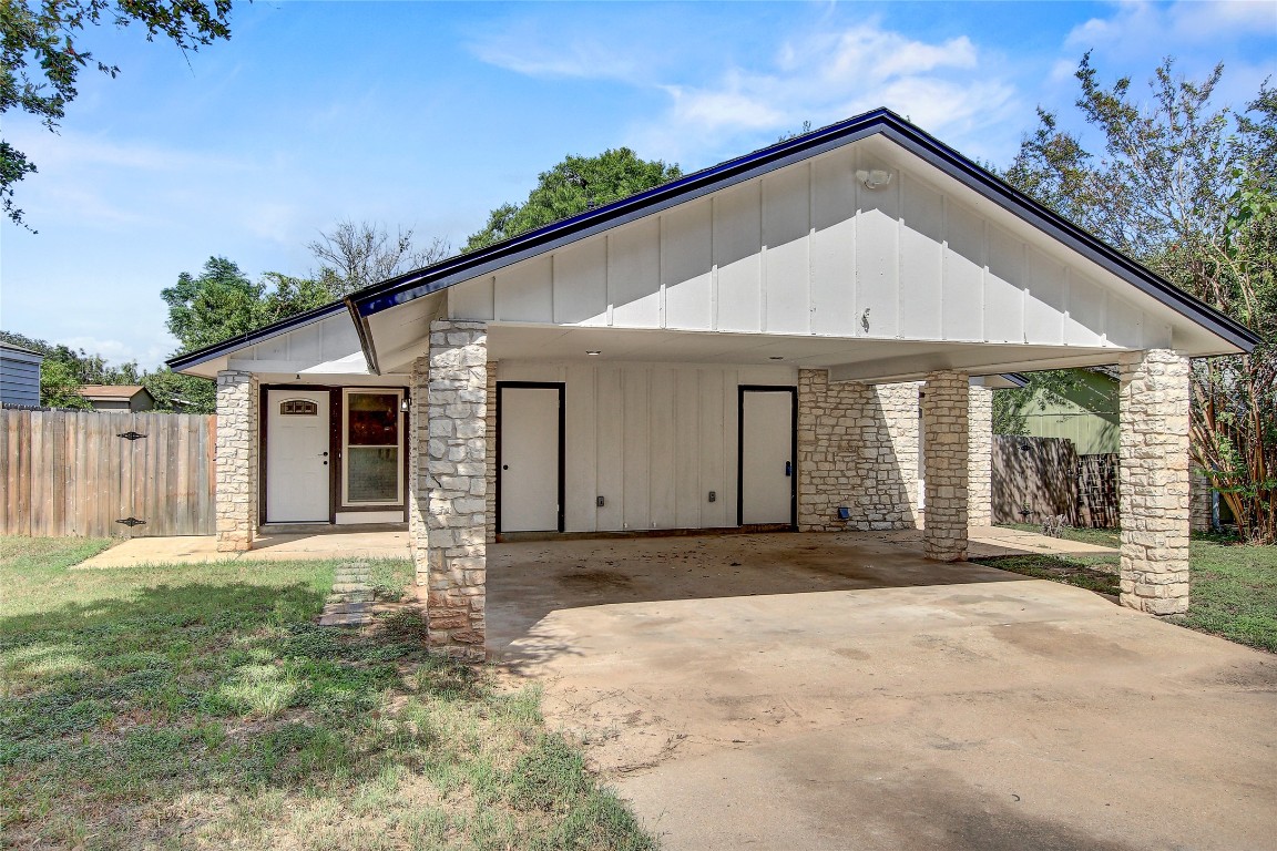 View of front of home with driveway, a patio area, board and batten siding, a carport, and stone siding