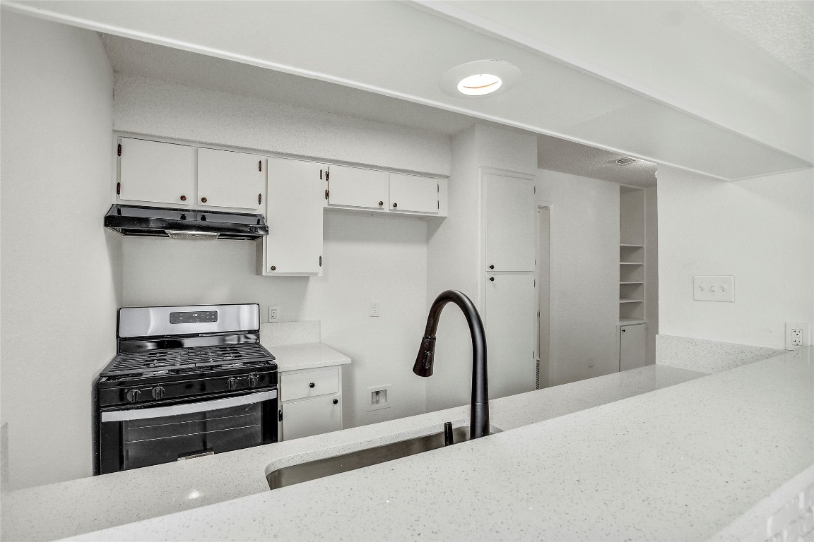 902 King Albert Street, Unit A Austin, TX 78745 - Photo 8 of 19 Kitchen with stainless steel range with gas stovetop, white cabinetry, under cabinet range hood, and light stone counters