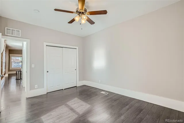 an empty room with wooden floor chandelier fan and windows