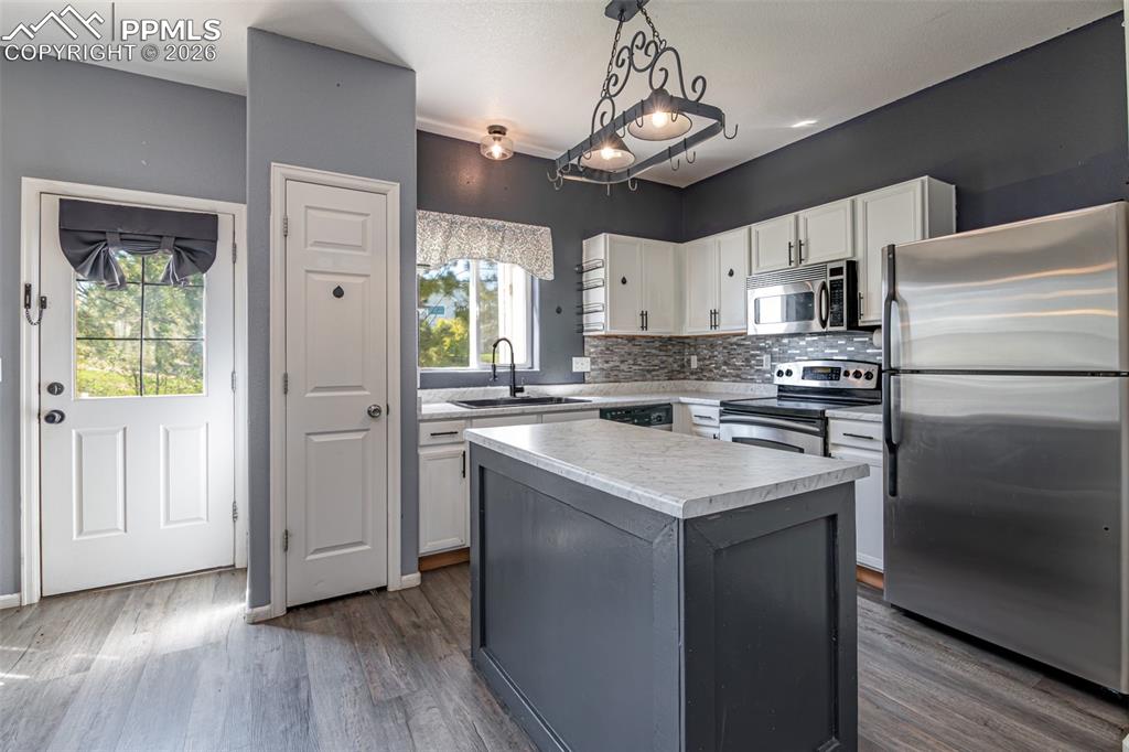 7740 Sandy Springs Point Fountain, CO 80817 - Photo 9 of 34 Two tone kitchen with stainless steel appliances, decorative backsplash, light countertops, pendant lighting, and a center island